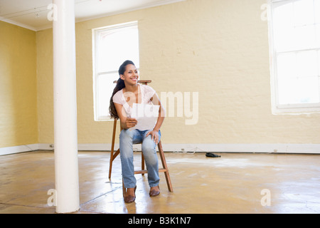 Frau sitzt auf Leiter im leeren Raum Papier halten Stockfoto