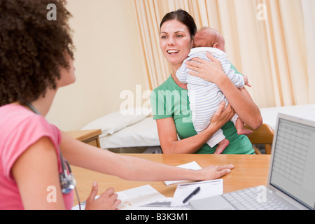 Arzt mit Laptop und Frau des Arztes Büro halten Baby Stockfoto