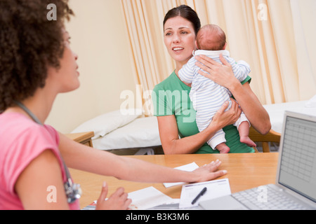 Arzt mit Laptop und Frau des Arztes Büro halten Baby Stockfoto