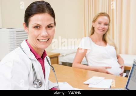 Arzt mit Laptop und Schwangere in Arztpraxis lächelnd Stockfoto