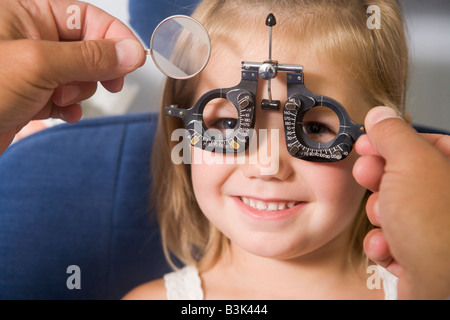 Optiker in Untersuchungszimmer mit jungen Mädchen im Sessel lächelnd Stockfoto