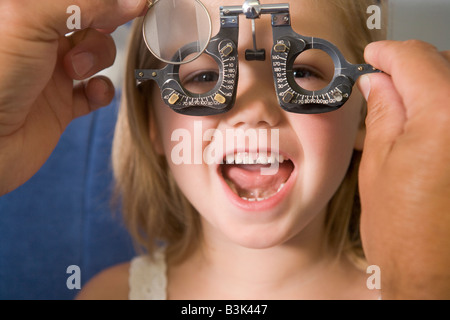 Optiker in Untersuchungszimmer mit jungen Mädchen im Sessel lächelnd Stockfoto