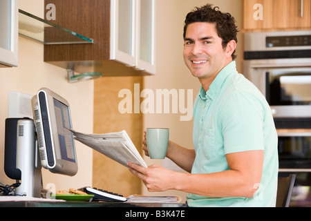 Mann in der Küche mit Computer Zeitung und Kaffee lächelnd halten Stockfoto