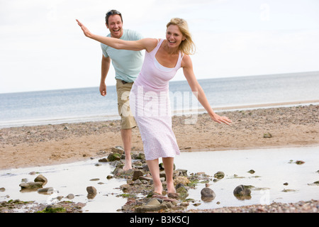 Paar am Strand zu Fuß auf Steinen und lächelnd Stockfoto