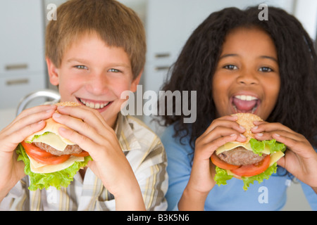 Zwei junge Kinder in Küche Essen Cheeseburger lächelnd Stockfoto