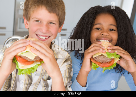 Zwei junge Kinder in Küche Essen Cheeseburger lächelnd Stockfoto