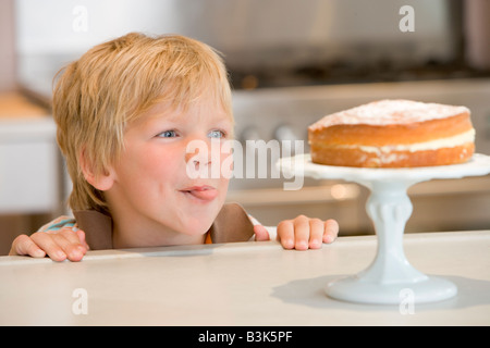 Kleiner Junge in Küche betrachten Kuchen auf Zähler Stockfoto