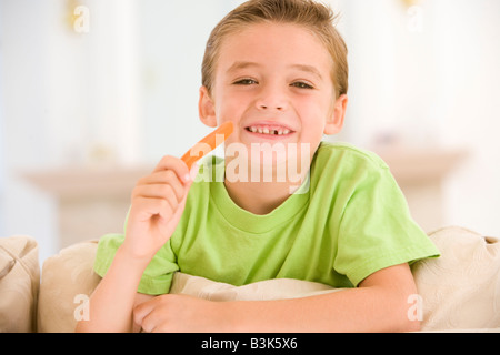 Kleiner Junge Essen Karotte Stick im Wohnzimmer lächelnd Stockfoto