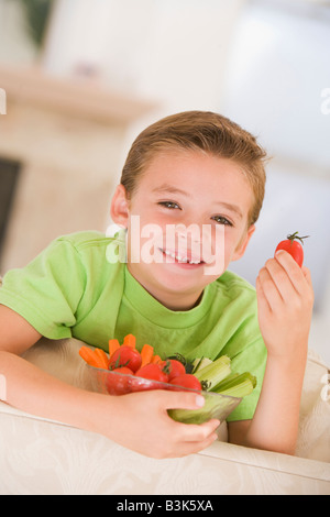 Kleiner Junge Essen Schale mit Gemüse im Wohnzimmer lächelnd Stockfoto