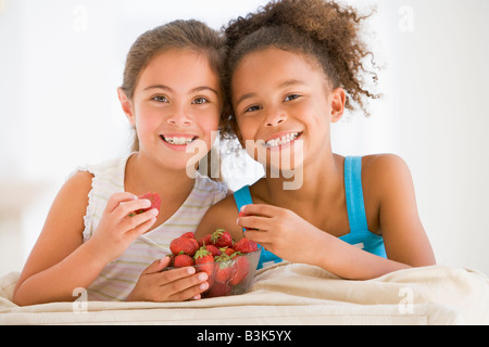 Zwei junge Mädchen essen Erdbeeren im Wohnzimmer lächelnd Stockfoto