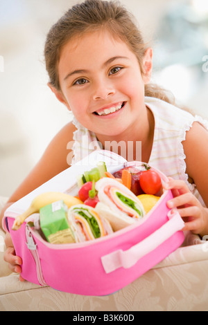 Junges Mädchen mit Lunchpaket im Wohnzimmer lächelnd Stockfoto