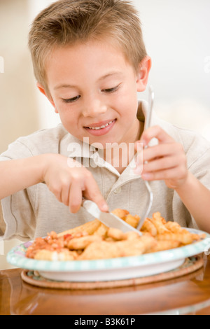 Kleiner Junge drinnen essen Fish &amp; Chips lächelnd Stockfoto