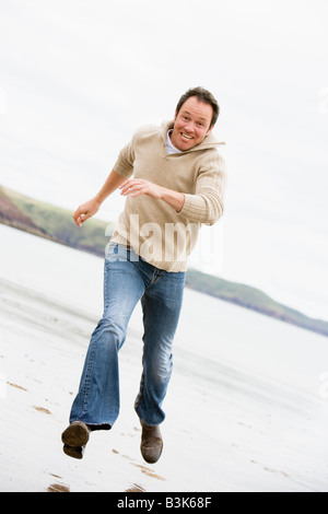 Mann läuft auf Strand lächelnd Stockfoto