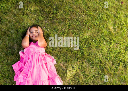 Eine kleine Inderin Denken während der Verlegung auf dem grünen Rasen. Stockfoto