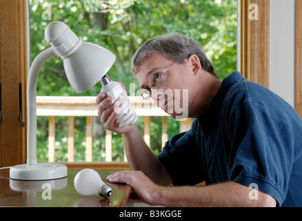 Ein 45 Jahre alter Mann ersetzt eine Haushalt weißglühende Glühlampe durch eine energiesparende kompakte Leuchtstofflampe Stockfoto