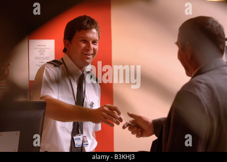 EIN GAST ANMELDET GEHOLFEN VON EINEM WACHMANN AN EINER HOTELREZEPTION UK Stockfoto