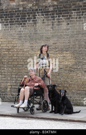 Frau drängen Mutter im Rollstuhl sitzen, während zwei Hunde zu Fuß Stockfoto
