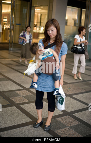 Frau mit Handy-Shops in Tokyo Japan Baby im Tragetuch tragen Stockfoto