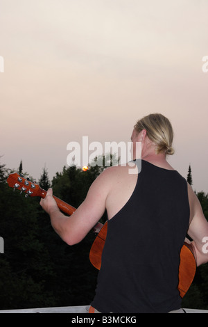 Der kaukasische junge Mann mit blonden, langen Haaren spielt auf Akustikgitarre Rückansicht Michigan MI Bilder Bilder Fotos vertikales Format in den USA Hi-res Stockfoto