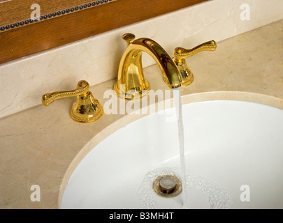 Wasser im Waschbecken aus goldenen Wasserhahn fließt Stockfoto