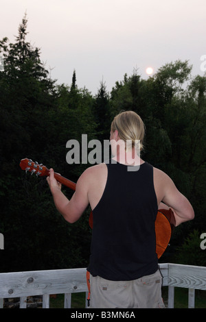 Der kaukasische junge Mann mit blonden, langen Haaren spielt auf Akustikgitarre Rückansicht Michigan MI Bilder Bilder Fotos vertikales Format in den USA Hi-res Stockfoto