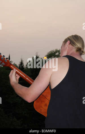Kaukasischer junger Mann blonde Haare spielen auf der Gitarre in Michigan MI USA US-Rückansicht von hinten szenische Person Sommer vertikales Format Hi-res Stockfoto