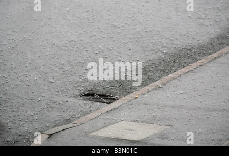 Regenwasser fließt in einen Abfluss an der Seite einer Straße in Redditch, Worcestershire UK während einem Sommergewitter Stockfoto