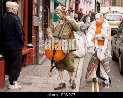 Straßentheater seltsamen Kostüm Musiker spielt Cello außen Kneipe Alter Mann mit Mütze Teil Gaelforce Kunst Festival Dumfries UK Stockfoto