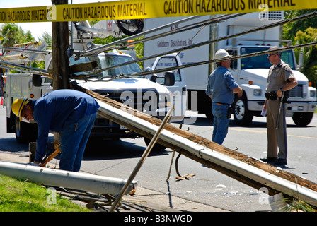 Elektriker und ein Polizist diskutieren die Situation der zerstörten Strommast nach ein SUV durch sie stürzte Stockfoto