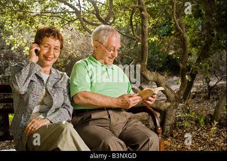 Senioren-Paar sitzt auf einer Bank auf dem Handy sprechen und lesen im park Stockfoto