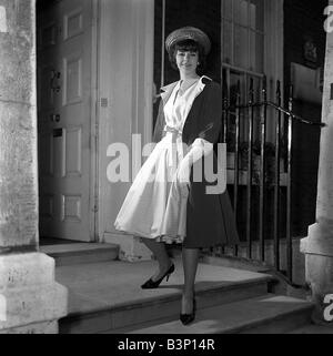 Ein Modell tragen eine Modedesign-Ausbildung in 1962 trägt einen langen Mantel über eine volle geschürzten Kleid stehen auf den Stufen zu einem Haus Stockfoto