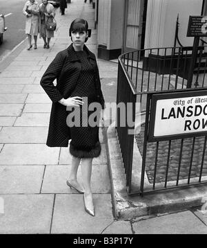 Sixties Fashion von Kiki Byrne Modell trug ein schwarzes Kleid mit passendem Mantel Stand an der Ecke von Lansdown Row in London mit der Hand auf ihre Hüfte Stockfoto