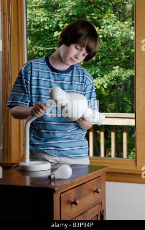 Ein elfjähriger Junge ersetzt eine Haushalt weißglühende Glühlampe durch eine energiesparende kompakte Leuchtstofflampe Stockfoto