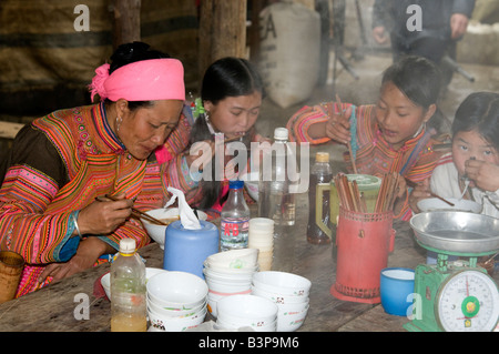 Eine Blume Hmong-Frau und ihre Kinder essen Dampfende Schüsseln mit Essen an einer Garküche in Bac Ha Markt Nord-Vietnam Stockfoto