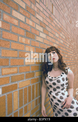 Junge Frau, die an eine Mauer gelehnt in Gedanken versunken Stockfoto