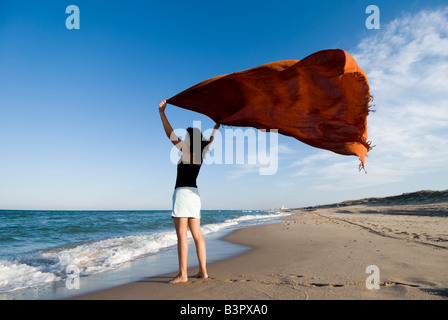 Model Released junge Frau hält einen Sarong in die Meeresbrise auf einem leeren Sandstrand Stockfoto