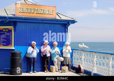 Vier weibliche Rentner, Essen zum Mitnehmen Fish &amp; Chips auf Llandudno Pier in Nord-Wales an einem sonnigen Tag Stockfoto