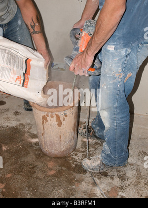 Zwei PUTZER MISCHEN TROCKENEN GIPS MIT WASSER MIT der Bohrmaschine mit Paddel in Container. MIX VERWENDET FÜR TROCKENE verkleideten Wänden Stockfoto