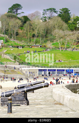 Gedenk-Kanone auf der Hafenmauer in Lyme Regis in Dorset mit strahlendem Sonnenschein und einem dunklen bewölkten Himmel Stockfoto