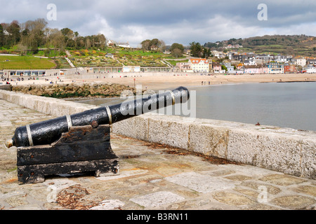 Gedenk-Kanone auf der Hafenmauer in Lyme Regis in Dorset mit strahlendem Sonnenschein und einem dunklen bewölkten Himmel Stockfoto