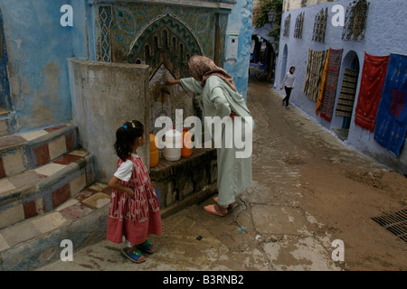 Frau füllt Wasser-Container aus Wasserhahn in der Straße von Chefchaouen. Viele Häuser in der Altstadt sind noch ohne fließendes Wasser Stockfoto