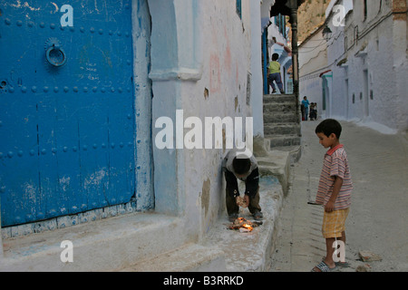 Kinder spielen mit dem Feuer in den gepflegten Straßen von Chefchaouen. Stockfoto