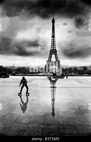 Ein einsamer Roller Skater vor dem Eiffelturm in Paris mit Gewitter brauen, spiegelt sich auf dem Pflaster. ca.. 1977 Stockfoto