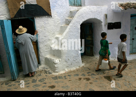 Mann in einem Jellabah Geschäfte wie zwei jungen vorbei in die engen Fußgängerzonen von Chefchaouen gehen. Stockfoto