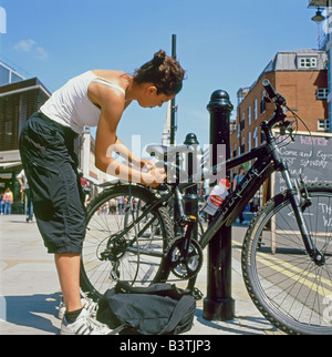 Eine weibliche Radfahrer ihr Fahrrad zu einem Hitching Post in Spitalfields, East End, London UK England KATHY DEWITT aufzuhängen Stockfoto