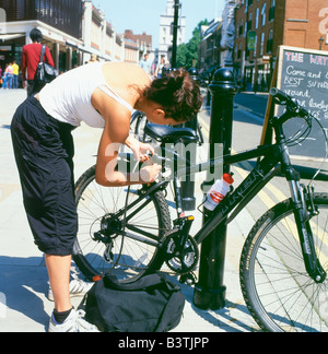 Eine weibliche Radfahrer ihr Fahrrad zu einem Hitching Post in Spitalfields, East End, London, England KATHY DEWITT sperren Stockfoto