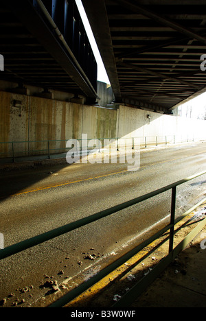 Die untergehende Sonne wirft lange Schatten unter einer Eisenbahnbrücke Stockfoto