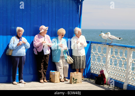 Vier weibliche Rentner, Essen zum Mitnehmen Fish &amp; Chips auf Llandudno Pier in Nord-Wales an einem sonnigen Tag Stockfoto