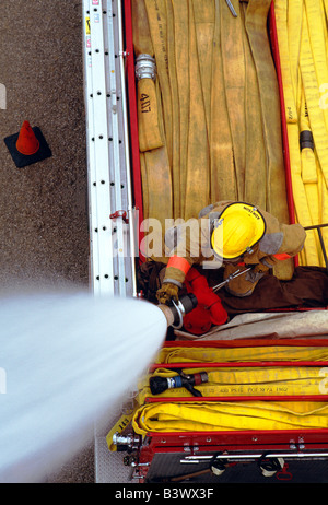 Draufsicht auf ein Feuerwehrmann auf ein Feuerwehrauto Besprühen mit Wasser aus dem Schlauch Stockfoto