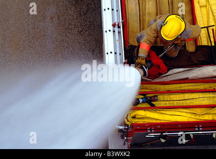 Draufsicht auf ein Feuerwehrmann auf ein Feuerwehrauto Besprühen mit Wasser aus dem Schlauch Stockfoto